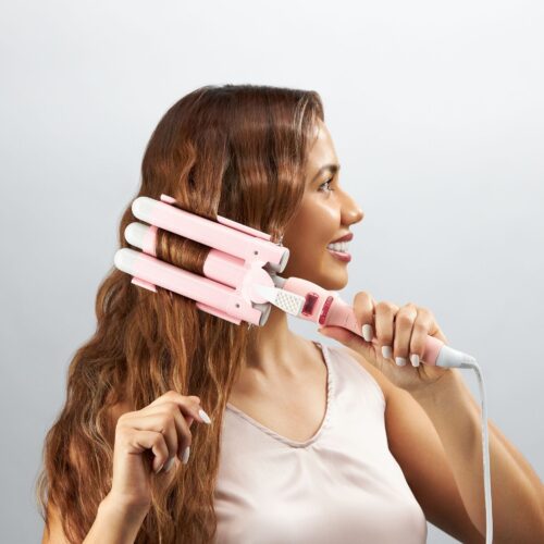 Action shot of a female hispanic model curling her hairs using pink curling iron.