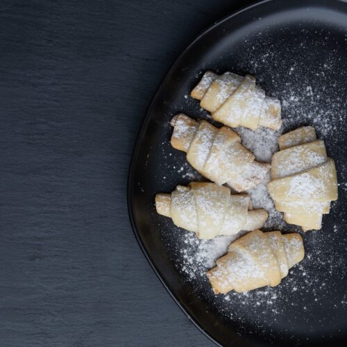 Food photography of croissants coated with powdered sugar placed on a black tray.