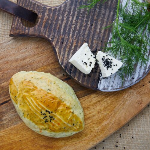 Food photography of a bread made of wheat , herbs and seeds placed on a wooden serving tray with some cheese and herbs on a wooden slider