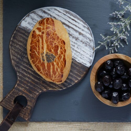 Food photography of a herb bread garnished with seeds placed on a wooden serving dish with side serving of black cherries