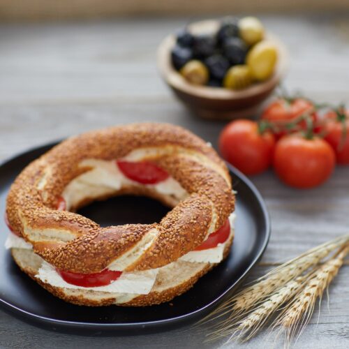 Food photography of a spiral cream cheese bagel with some sliced tomatoes filling placed on a black china plate and some some tomatoes and wheat in the background to add the beauty in the picture