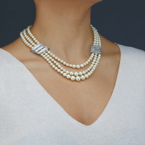Jewelry photography of a female model wearing a necklace and V-neck top on a gray background.