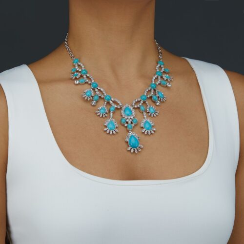 Female model wearing a necklace with blue stones and a white top.