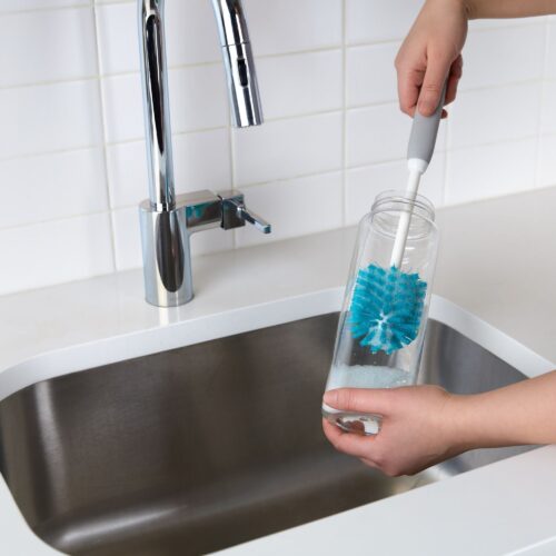 Female hand model cleaning a jar with scrub brush in the sink.