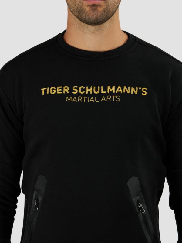 Half body shot of a male model wearing sweat shirt in black with a “ Tiger Schulmann’s martial arts” text in gold color.
