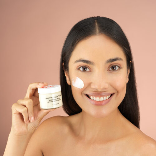 Cosmetics photography with female model holding a beauty cream in her hand and a swatch of the product is placed on her face.