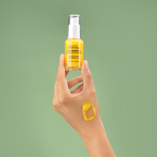 Creative lifestyle photography of a female hand model holding antioxidant serum and a cosmetic swatch on her hand shot on a green background.