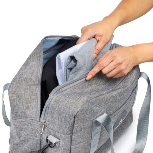 White background action shot of a female hand model putting clothes inside a travel bag.