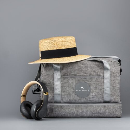 Skin colored textured hat with black strip placed on a travel bag and black headphones placed alongside it, shot on a gray background.