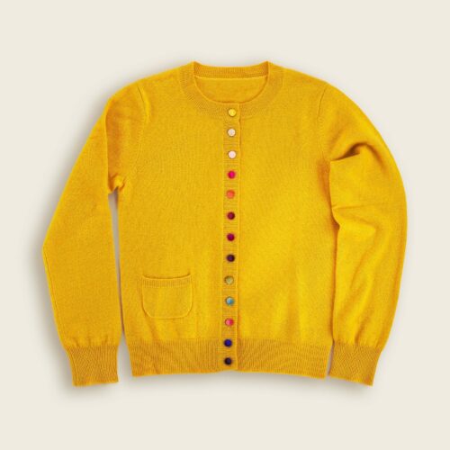 Lay flat apparel photography of a yellow sweater with multi color buttons placed on a white background.