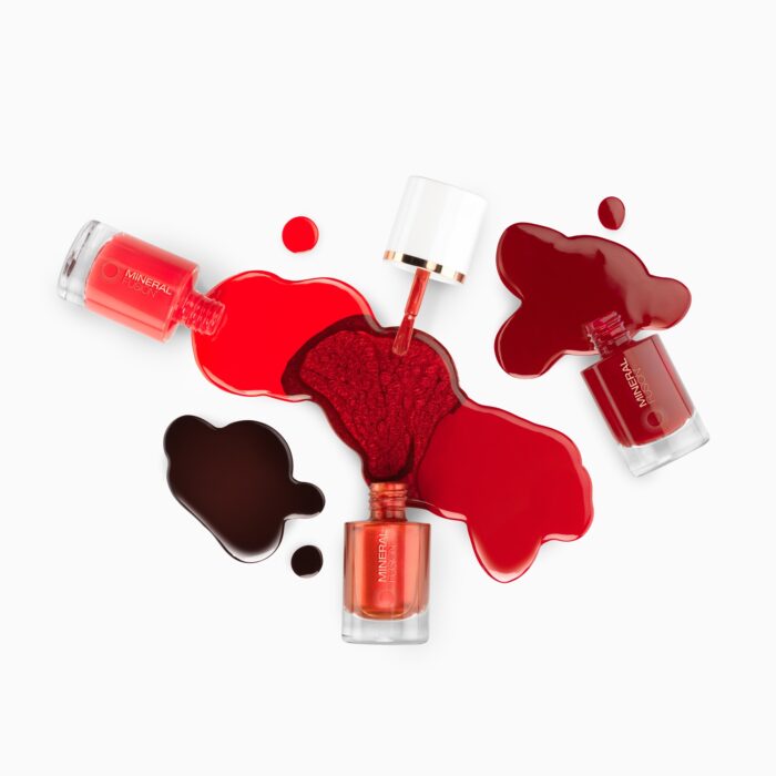 Creative cosmetics photography of three nail polish bottles with different shades of red.