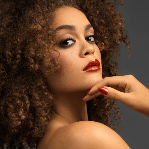 Beauty shot of a black female model with curly hairs wearing red nail polish and lipstick. Shot by Commercial Photographer Isa Aydin.